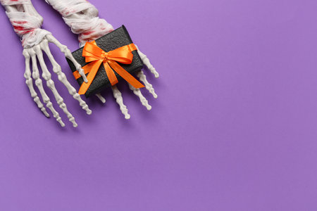 Skeleton hands with gift box for Halloween celebration on purple backgroundの写真素材