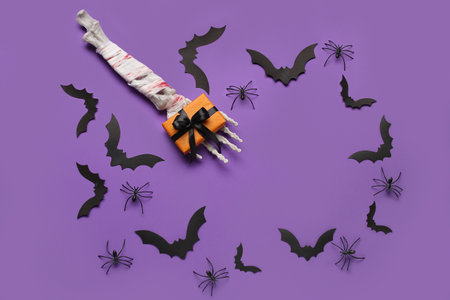 Frame made of skeleton hand, gift box, paper bats and spiders for Halloween celebration on purple backgroundの写真素材