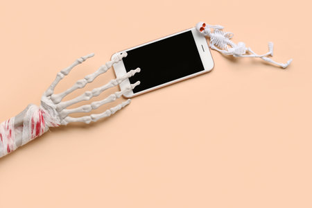 Skeleton with hand and modern mobile phone for Halloween celebration on beige backgroundの写真素材