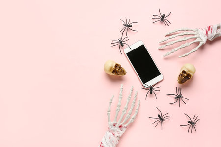 Skeleton hands with modern mobile phone, skulls and spiders for Halloween celebration on beige backgroundの写真素材