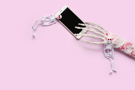 Skeletons with hand and modern mobile phone for Halloween celebration on pink backgroundの写真素材