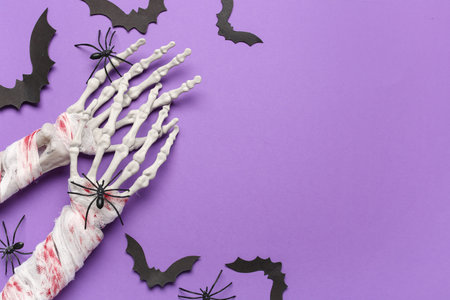 Skeleton hands with spiders and paper bats for Halloween celebration on purple backgroundの写真素材