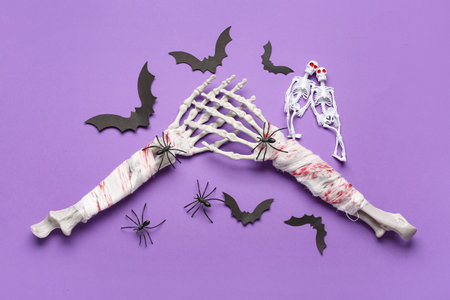 Skeletons with hands, paper bats and spiders for Halloween celebration on purple backgroundの写真素材