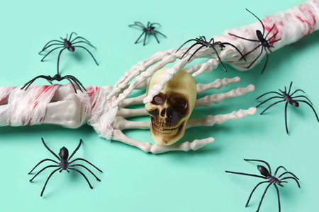 Skeleton hands with skull and spiders for Halloween celebration on turquoise background, closeupの写真素材