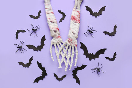 Composition with skeleton hands, spiders and paper bats for Halloween celebration on purple backgroundの写真素材