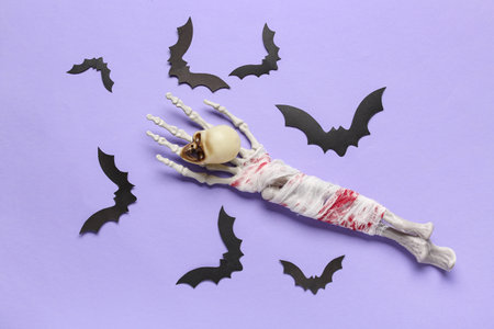 Skeleton hand with skull and paper bats for Halloween celebration on purple backgroundの写真素材
