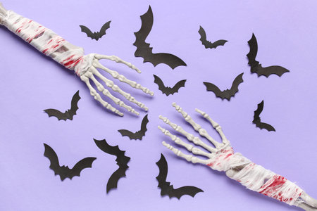 Composition with skeleton hands and paper bats for Halloween celebration on purple backgroundの写真素材