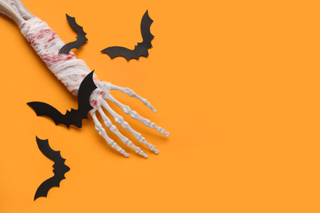 Skeleton hand and paper bats for Halloween celebration on orange backgroundの写真素材