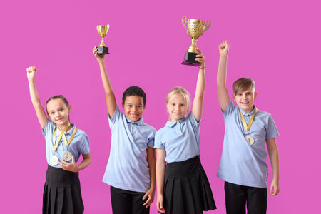 Smart little classmates in stylish uniform with prize cups and medals on purple backgroundの写真素材