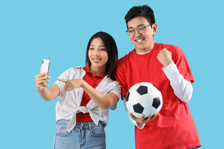 Young Asian friends with mobile phone and soccer ball on blue backgroundの写真素材