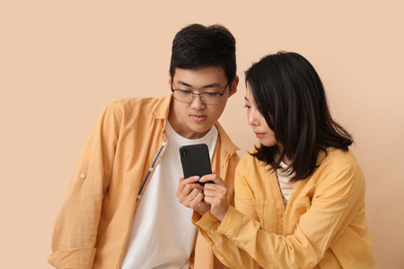 Young Asian friends using mobile phone on beige backgroundの写真素材