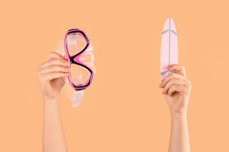 Female hands with mini surfboard and snorkeling mask on orange backgroundの写真素材