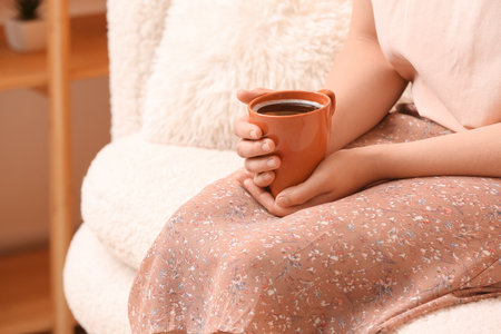 Woman with cup of tasty coffee resting on sofa at homeの写真素材