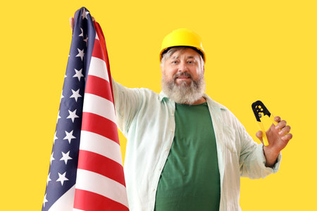 Portrait of senior man in hardhat with wire crimper and USA flag on yellow background. labor day celebrationの写真素材