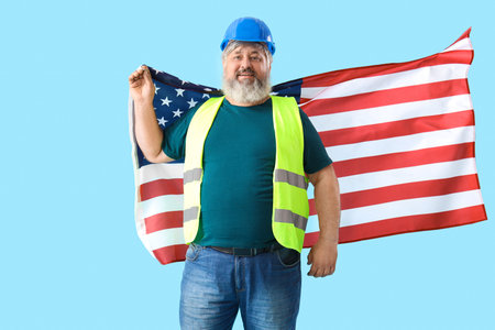 Portrait of happy senior man in hardhat with USA flag on blue background. labor day celebration