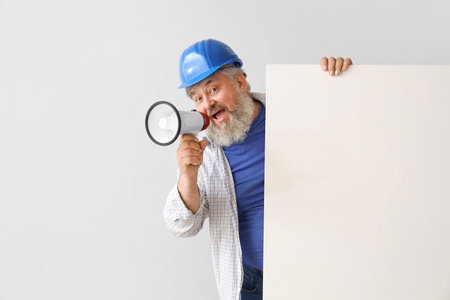 Portrait of senior man in hardhat with blank poster and megaphone on gray background. labor day celebrationの写真素材