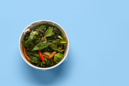 Bowl of fresh salad covered with plastic food wrap on blue backgroundの写真素材