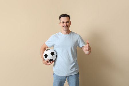 Handsome man with soccer ball showing thumb-up on beige backgroundの写真素材