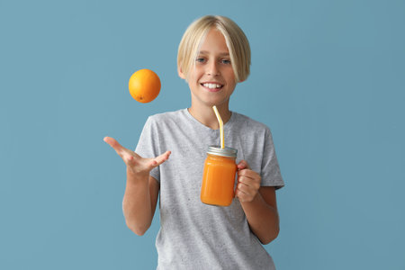 Little boy with glass jar of juice and orange on blue backgroundの写真素材