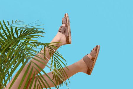 Female legs in stylish sandals with palm leaves on blue backgroundの写真素材