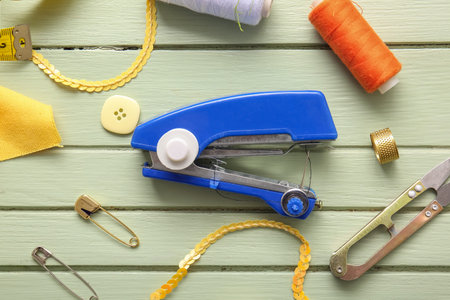 Manual sewing machine with different supplies on green wooden background