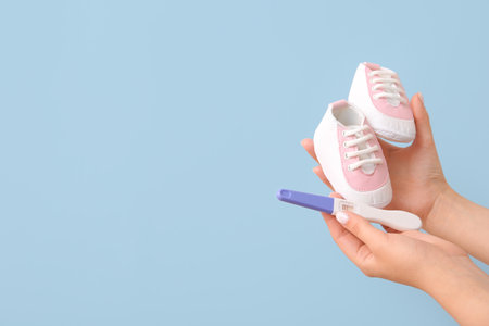 Female hands with positive pregnancy test and baby booties on color backgroundの写真素材