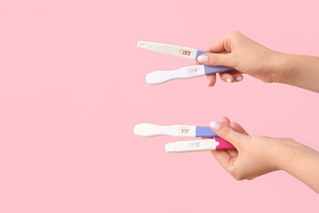 Female hands with different pregnancy tests on pink backgroundの写真素材