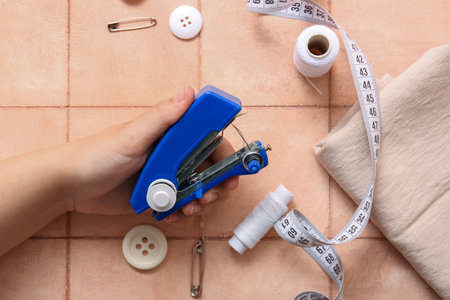 Female hand with different supplies and manual sewing machine on pink tile backgroundの写真素材