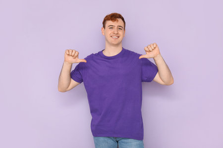 Young man pointing at his purple t-shirt on lilac backgroundの写真素材
