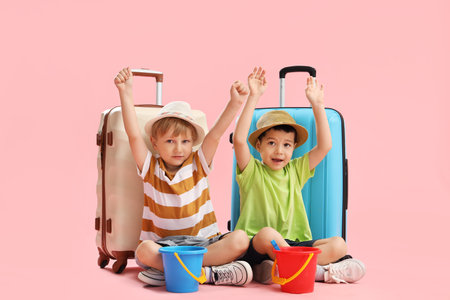 Cute little boys with beach toys and suitcases on pink backgroundの写真素材