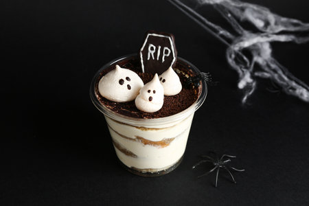 Plastic cup with delicious tiramisu and web for Halloween celebration on dark background, closeupの写真素材