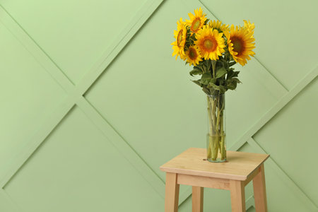 Vase with beautiful sunflowers on stool near green wall in roomの写真素材