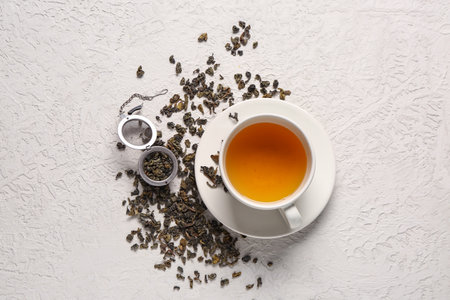 Cup of tea with infuser and dry green tea leaves on white textured backgroundの写真素材