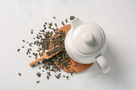 Teapot, wooden scoop and board with green tea leaves on white backgroundの写真素材