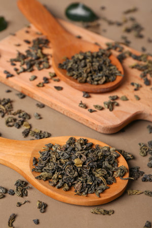 Wooden spoons and board with green tea leaves on brown backgroundの写真素材