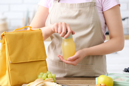 Woman bottle packing of juice into lunch box bag in kitchenの写真素材