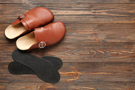 Pair of leather slippers and orthopedic insoles on wooden backgroundの写真素材