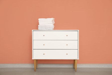 Stack of clean towels on chest of drawers near color wall