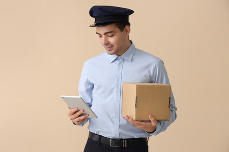 Young postman with tablet computer and parcel on beige backgroundの写真素材