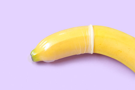 Fresh banana in condom on purple background, closeup. sex education conceptの写真素材