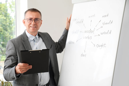 Male teacher with clipboard conducting English grammar lesson in classroomの写真素材