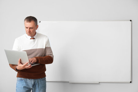 Male teacher with laptop near flipboard in classroomの写真素材
