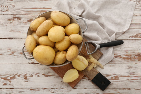 Colander and board with raw potatoes on white wooden backgroundの写真素材