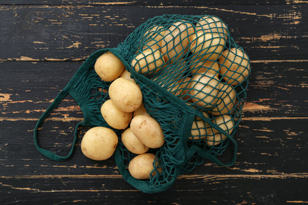 String bag with raw potatoes on black wooden backgroundの写真素材