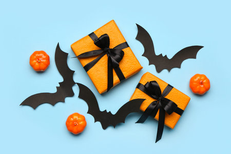Paper bats with pumpkins for Halloween party and gift boxes on blue background