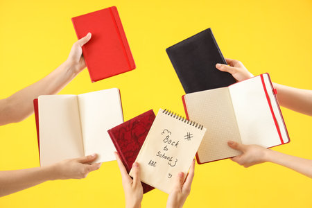 Many female hands holding notebooks with text BACK TO SCHOOL on yellow backgroundの写真素材