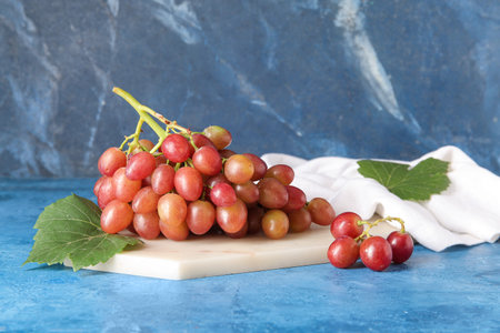 Board with tasty ripe grapes on blue background
