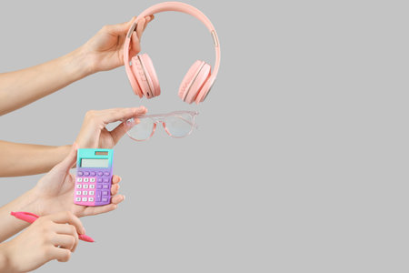 Female hands with headphones, calculator and eyeglasses on gray backgroundの写真素材