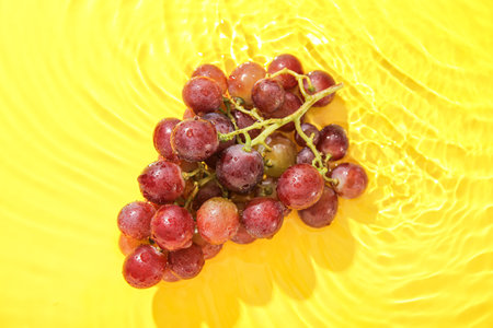 Tasty ripe grapes in water on yellow backgroundの写真素材
