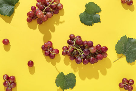Tasty ripe grapes with leaves on yellow background